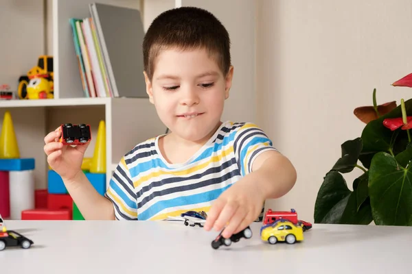 Anaokulu çocuğu evde bir masada oyuncak arabalarla oynuyor..