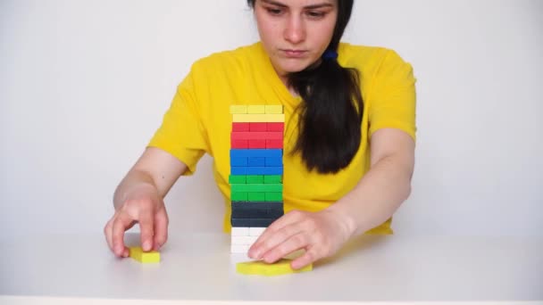 A woman in a yellow T-shirt plays jenga, builds a tower of colorful wooden blocks. 14 May 2022, Zaporozhye, Ukraine — Vídeo de Stock