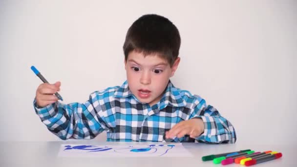 A 4-year-old boy coloring a drawing and talking looking into the camera on a white background. — Wideo stockowe