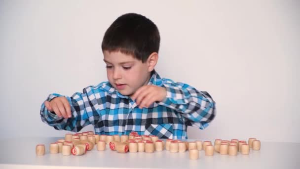 A preschool boy plays lotto, folds barrels with numbers on the table. The child learns to count — Stock videók