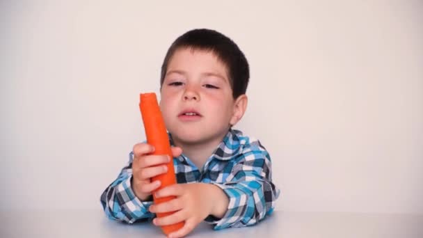 Een 4-jarige jongen eet wortelen op een witte achtergrond. Harde groenten voor tandheelkundige gezondheid bij kinderen. — Stockvideo