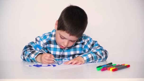 Uma criança pré-escolar em uma camisa xadrez desenha um desenho, tintas com um marcador azul — Vídeo de Stock