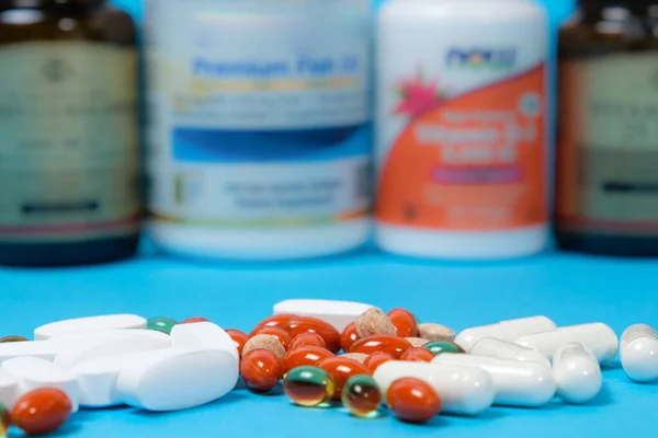 Cápsulas y pastillas blancas y naranjas sobre fondo azul, frascos con suplementos dietéticos sobre fondo —  Fotos de Stock