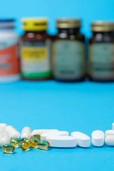 Medicamentos o suplementos dietéticos en un fondo azul y frascos con pastillas en el fondo. —  Fotos de Stock