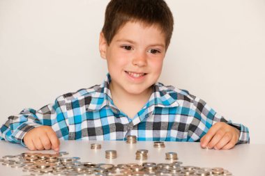 A preschool boy in a plaid shirt counts coins, builds towers. Financial literacy for children. clipart