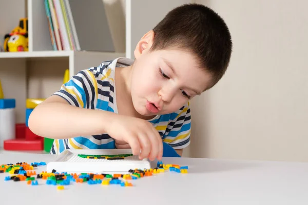 Chłopiec w wieku 4 lat bawi się mozaiką, zbiera obraz z małych plastikowych części. Rozwój umiejętności motorycznych u dzieci — Zdjęcie stockowe
