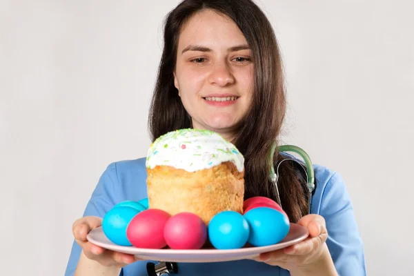 Läkaren håller en påskkaka och målade ägg och leenden på en vit bakgrund. — Stockfoto