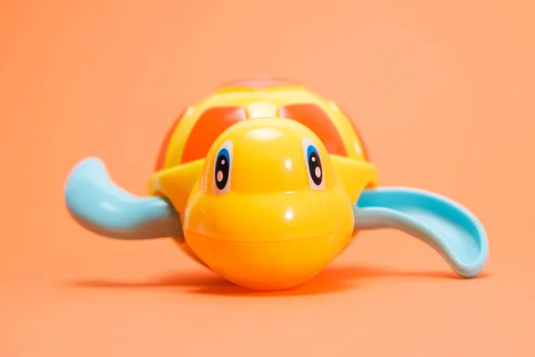 Yellow plastic turtle for playing in the water on an orange background. Toys for babies for bathing. — Stock Photo, Image