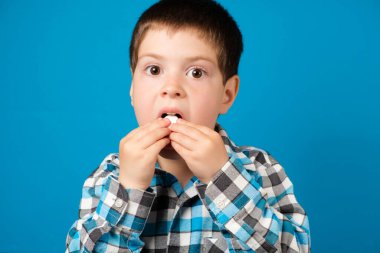 Güzel bir anaokulu çocuğu mavi arka planda C vitamini, ilaç ya da diyet takviyesi yer..