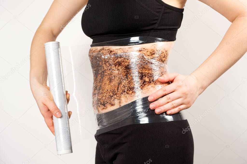 A woman makes a belly wrap with a coffee anti-cellulite body scrub. The concept of weight loss and skin care.