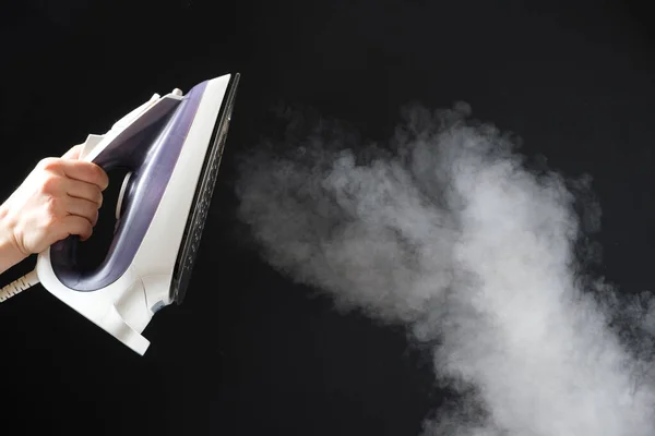 An iron with a steam generator sprays white hot steam on a black background. Steaming clothes, ironing