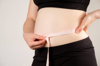 Bir kadın karın çevresini bir santimetre bant ile ölçer, yakın plan. Zayıflama konsepti.