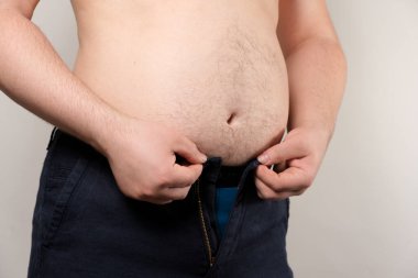 Bir adam dar pantolonunu bağlamaya çalışır. Erkek obezite konsepti, aşırı ağırlık.