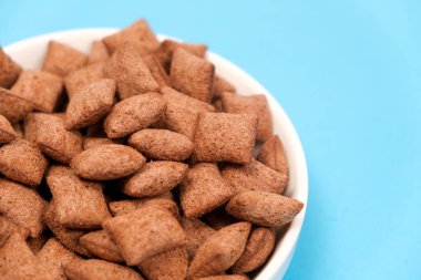 Tatlı kahvaltı gevreği kuru - mısır gevreğinden yapılmış çikolata pedleri mavi arka planda, kenar manzaralı.