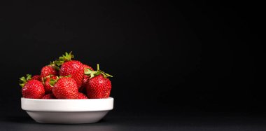 Siyah arka planda beyaz tabakta kırmızı taze çilekler. Yaz mevsimlik meyveler, yakın plan..
