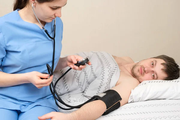 The doctor measures the blood pressure of a young 30-year-old man lying in bed. Diseases of the heart and blood vessels in humans, mechanical tonometer