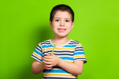 4 yaşında yakışıklı bir çocuk yeşil ekran arka planında diş fırçası tutuyor, metin için boşluk kopyalıyor..