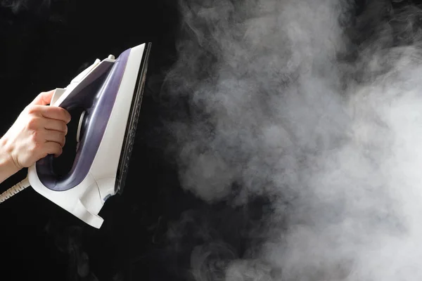 An iron with a steam generator sprays white hot steam on a black background. Steaming clothes, ironing