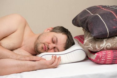 Ortopedik yastıkta uyuyan bir adam tüylü ve sentetik yastıklardan yapılma diğer yastıklar yerine hafıza köpüğüyle uyur.