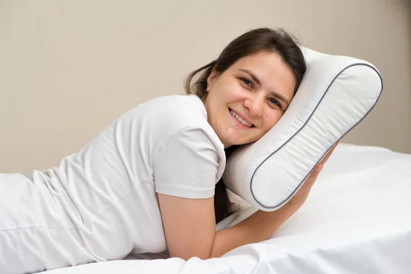 A woman holds an orthopedic pillow made of memory foam and smiles. Choosing the right pillow for healthy sleep