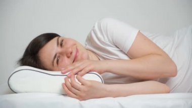 Hafıza köpüğünden yapılmış ortopedik yastığa uzanmış bir kadın kameraya bakıp gülümsüyor..