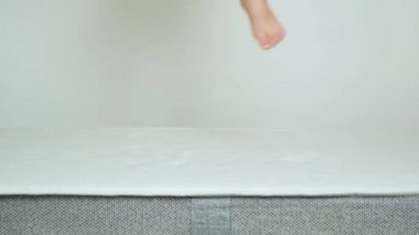 Küçük bir çocuk beyaz arka planda bir yatakta yükseğe zıplıyor..