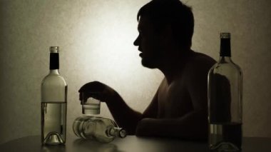 Alkolik bir adam votka içiyor şişelerle bir masada oturuyor, siluet video..