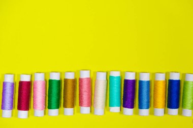 Sarı arkaplandaki yazı için boş bir alanı olan çok renkli iplikler seti, üst görünüm. Terzilik ve dikiş malzemeleri, terzi afişi