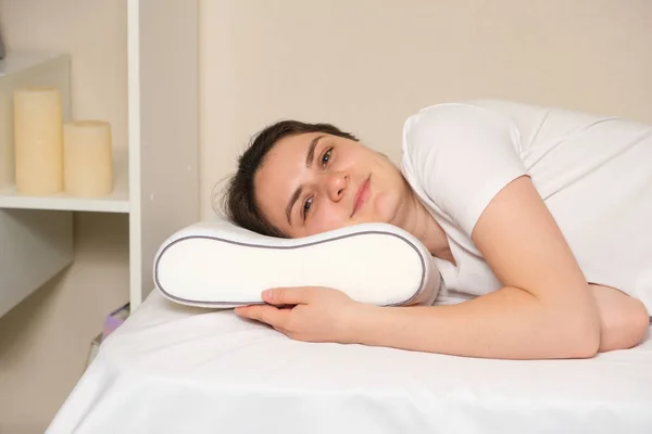 A woman lies on an orthopedic pillow, looks into the camera and smiles