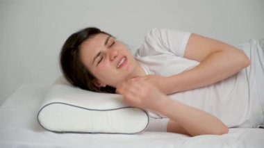 Bir kadın ağrılı bir boyunla uyanır, yastığını fırlatır ve karnının üstünde yatar.