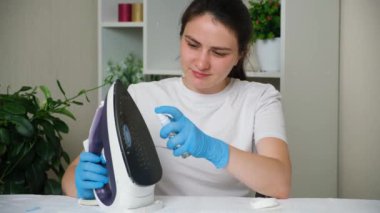 The housewife sprays a special solution on the dirty sole of the iron. Cleaning the iron from contaminants