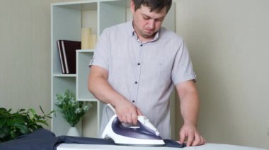 A man irons his shirt with an iron on an ironing board. Bachelor life, a mans housework