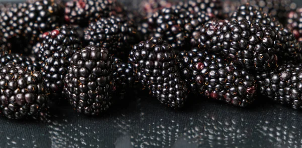 Blackberries on a black glass background are reflected in the glass, long banner