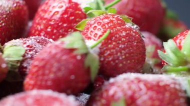 Çilekler şekerle serpilmiş siyah bir arka planda daire şeklinde dönerler..