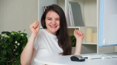 Bir kadın bilgisayar başında çalışırken ellerini çırpıyor ve dans ediyor.