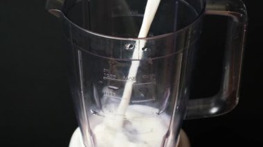 The process of pouring milk into the bowl of a blender for making a milkshake