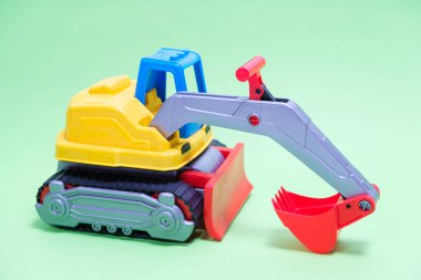 Yeşil arka planda sarı kazıcı plastik araba. Oyuncakçı ve çocuklar için kazı yapan inşaat makineleri.