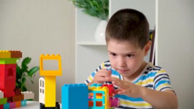 A boy of 5 years old plays as a constructor, builds from multi-colored cubes.