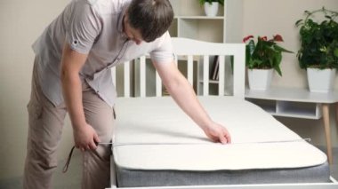 A man measures with a tape measure the width of an orthopedic mattress.