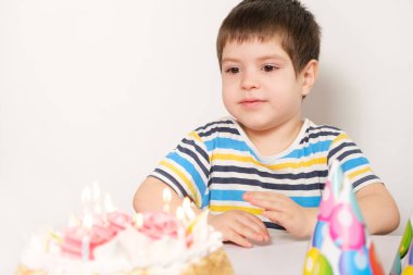 Yakışıklı bir çocuk doğum gününü kutlar, elinde mumlarla bir pastanın önüne oturur ve dilek tutar..