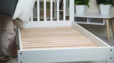 A man installs a mattress on a children's single wooden bed