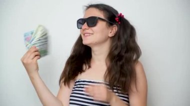 A young cheerful woman in sunglasses waves money like a fan