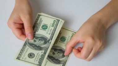 A woman counts dollar bills for 100 dollars on a white background, top view.