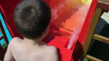 A 5-year-old boy jumps and watches the water flow on the slide in the aqua park