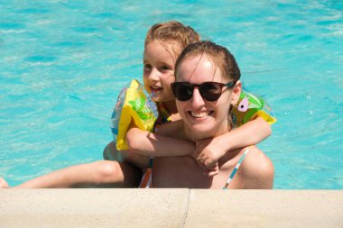 Mother and daughter are having fun in the pool, a girl with sleeves is learning to swim