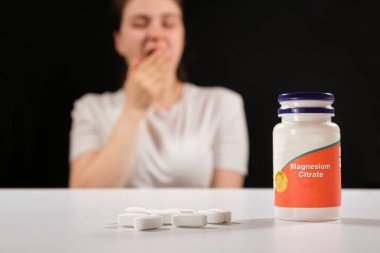Yorgun bir kadın ve bir kavanoz magnezyum sitrat. Yorgunluk, asabiyet ve uykusuzluk için besin takviyeleri..