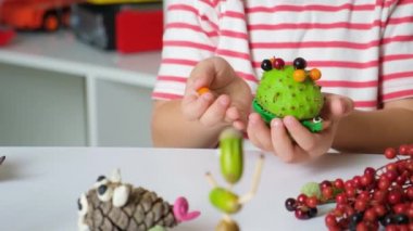 A 5-year-old boy plays with a chestnut hedgehog figure. Autumn crafts with your own hands.