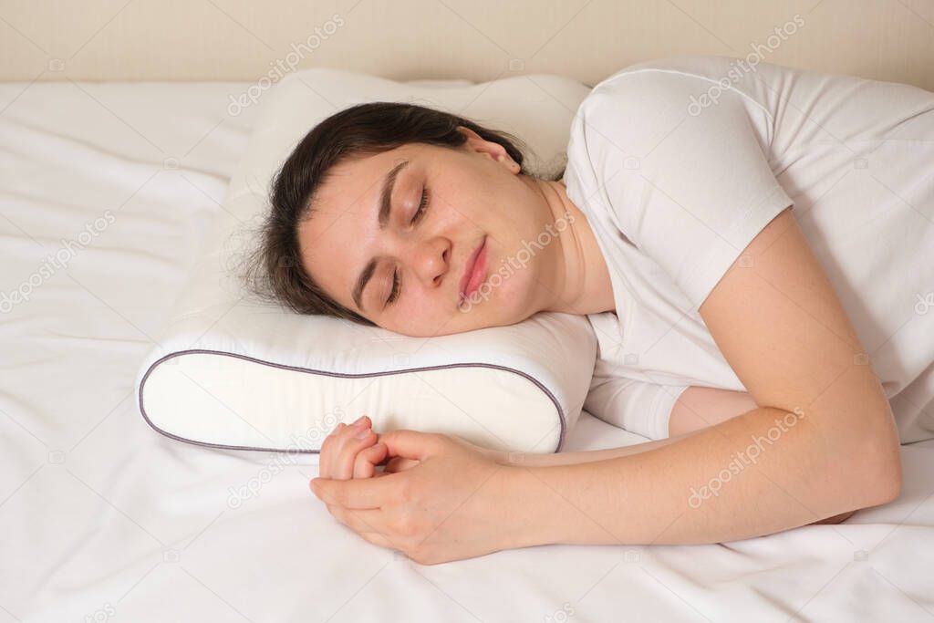 A woman sleeps on an orthopedic pillow made of memory foam, lying on a bed. The correct pillow for a comfortable healthy sleep
