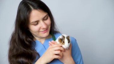 Veteriner elinde küçük bir kobay tutuyor, okşuyor ve gülümsüyor..