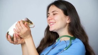 Veteriner elinde küçük bir kobay tutuyor, okşuyor ve gülümsüyor..